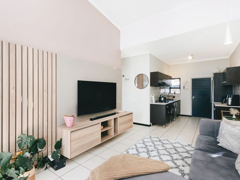 Open-plan living area featuring tiled flooring, a feature wall with vertical timber slats, and an adjoining kitchen with dark cabinetry.