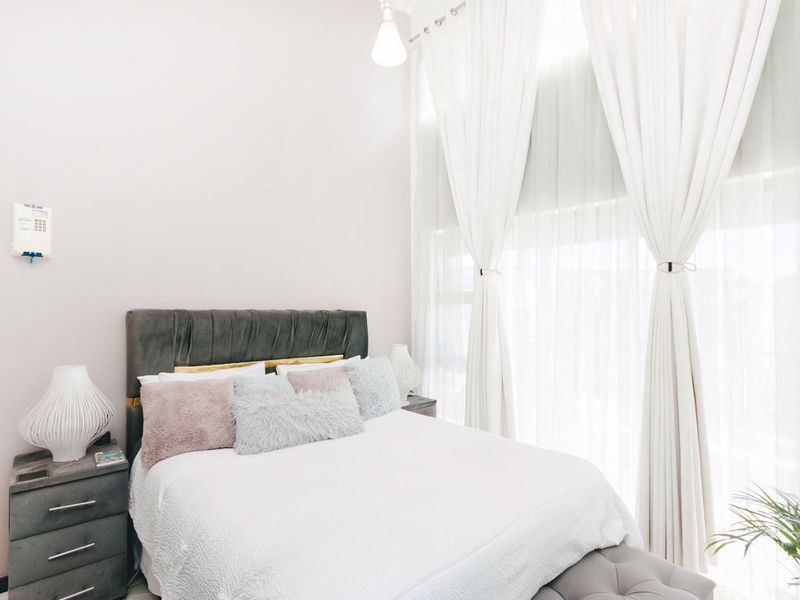 A bright and airy bedroom featuring high ceilings, large windows with floor-to-ceiling curtains, and a neutral color palette.