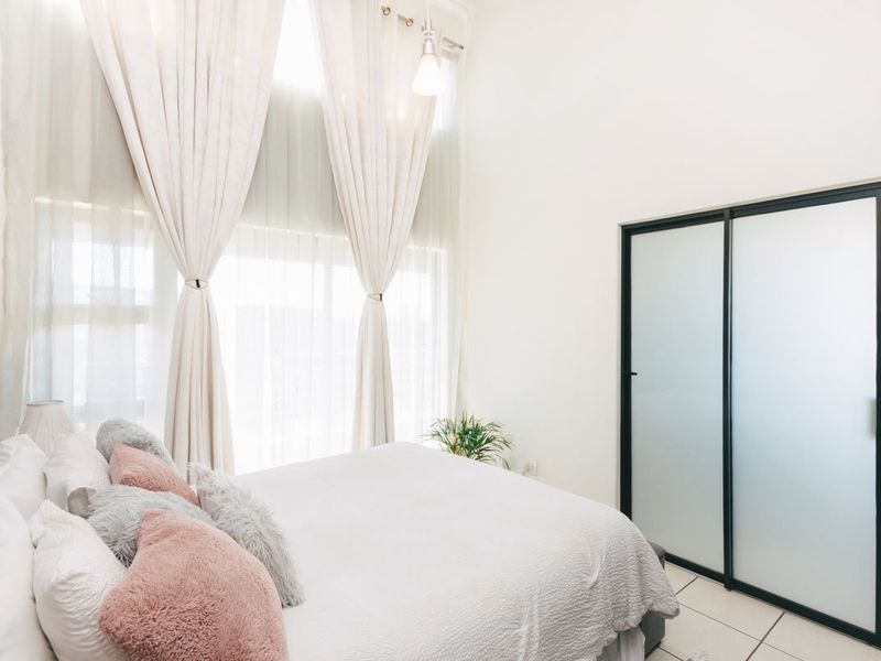 A bright bedroom featuring high ceilings, floor-to-ceiling windows with curtains, and modern sliding glass closet doors.