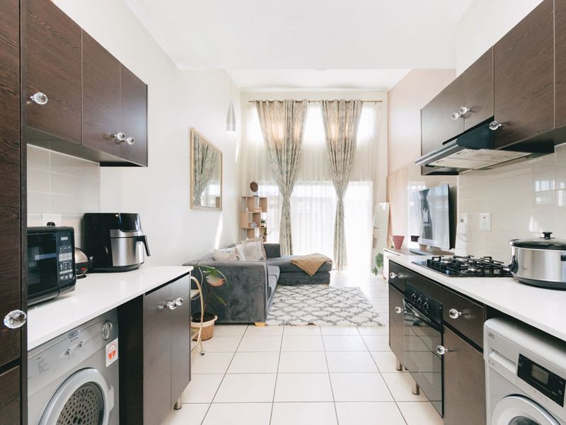 An open-plan apartment layout featuring a galley-style kitchen with dark cabinetry, integrated appliances, and a bright, connected living area with high ceilings.