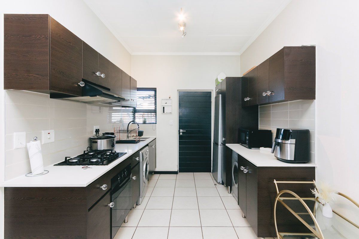 A functional galley-style kitchen featuring dark wood cabinetry, white countertops, a built-in gas hob, oven, and integrated laundry appliance space.