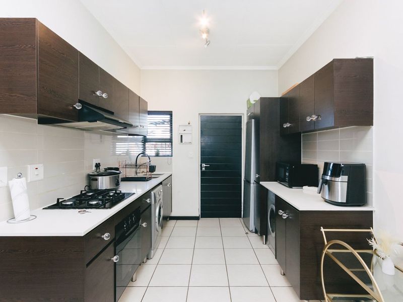 A functional galley-style kitchen featuring dark wood cabinetry, white countertops, a built-in gas hob, oven, and integrated laundry appliance space.