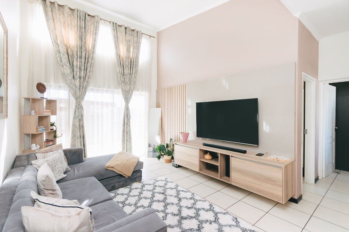 A bright living room featuring high ceilings, large windows with floor-to-ceiling curtains, and a modern built-in media wall with timber slat detailing.