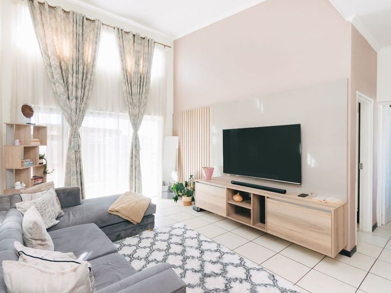 A bright living room featuring high ceilings, large windows with floor-to-ceiling curtains, and a modern built-in media wall with timber slat detailing.