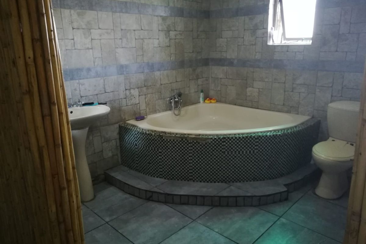 A bathroom featuring a corner bathtub with mosaic tiling, a pedestal basin, and a toilet, finished with textured wall tiles and floor tiling.