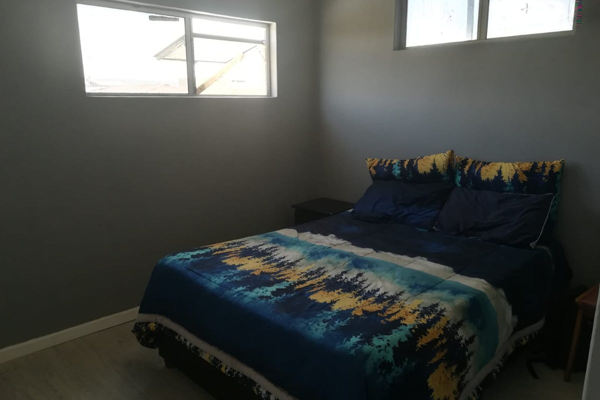 A bedroom featuring light-toned flooring, grey walls, and high-set windows providing natural light.