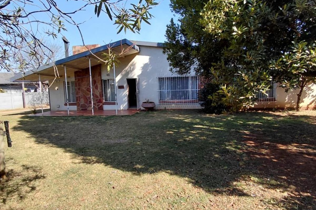 A single-story residential property featuring a covered patio, stone accent wall, and security bars on windows, set within a spacious garden area.
