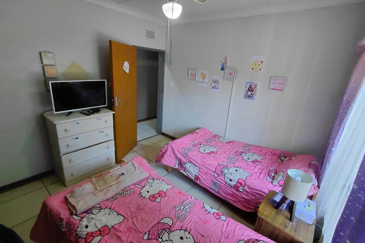 A functional bedroom featuring tiled flooring, a ceiling fan with integrated lighting, and a doorway leading to an adjacent hallway.