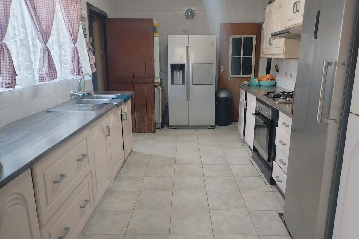A functional kitchen featuring tiled flooring, built-in cabinetry, a stainless steel oven, gas hob, and a double sink with tiled splashbacks.