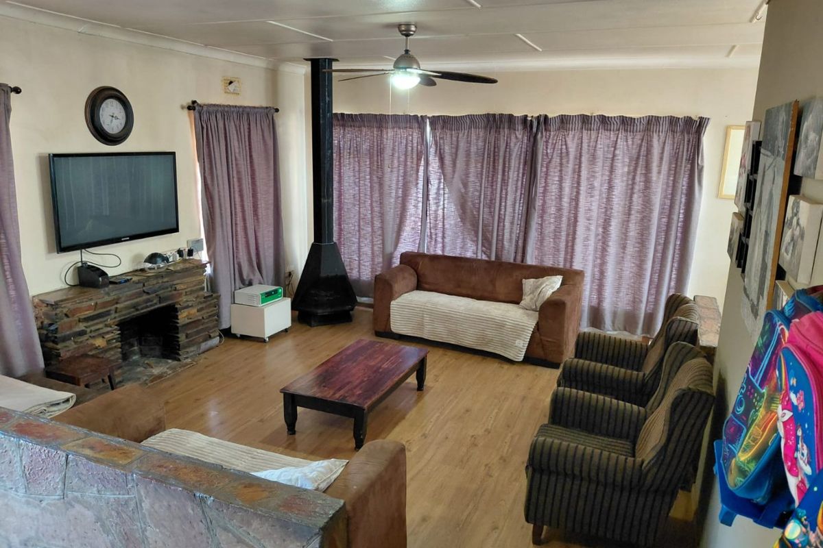 Spacious living room featuring a stone-clad fireplace, wood-burning stove, ceiling fan, and laminate flooring.