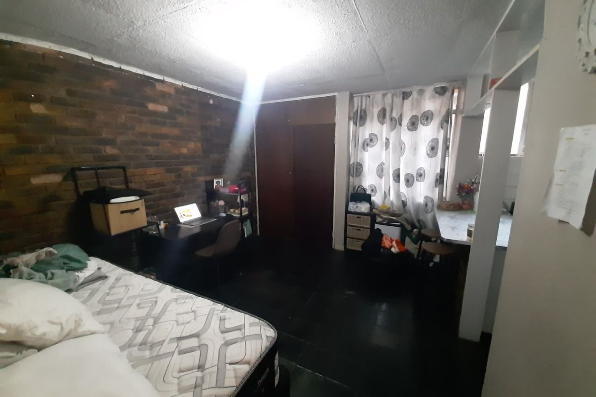 A bedroom featuring a dark brick feature wall, tiled flooring, and built-in shelving, offering a functional space with potential for modernization.