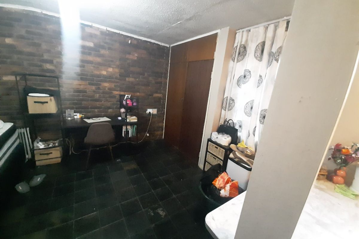 A bedroom featuring a dark brick feature wall, built-in wooden cupboards, and dark floor tiles, offering a functional space with potential for modernization.