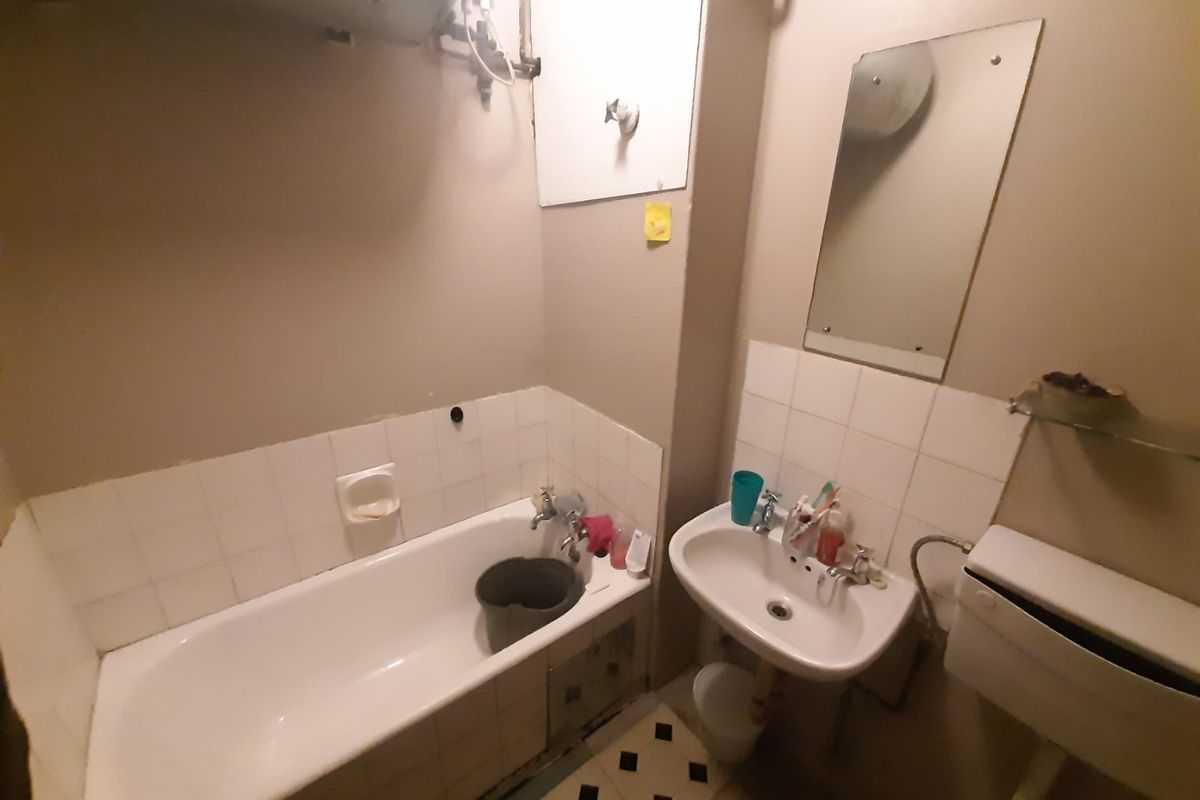 A compact bathroom featuring a standard bathtub, wall-mounted basin, and toilet, requiring modernization of finishes and fixtures.