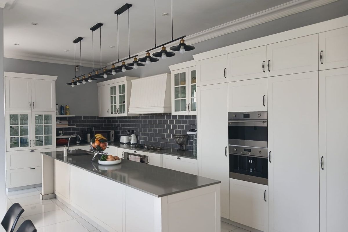Modern kitchen featuring white cabinetry, a large central island with stone countertops, dark subway tile backsplash, and integrated stainless steel appliances.