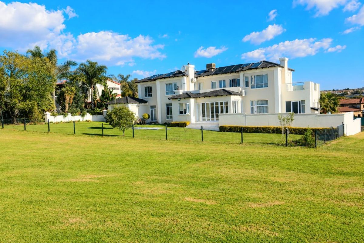 A spacious rear view of a large, multi-story residential property featuring a well-maintained lawn, landscaped garden, and expansive patio area.