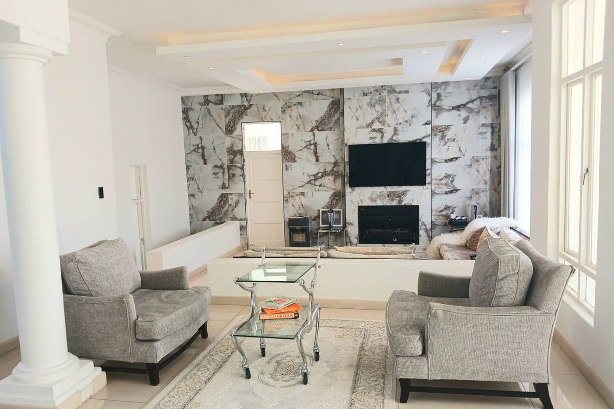 Spacious living room featuring a striking marble-tiled feature wall, built-in fireplace, recessed tray ceiling with integrated lighting, and large windows.