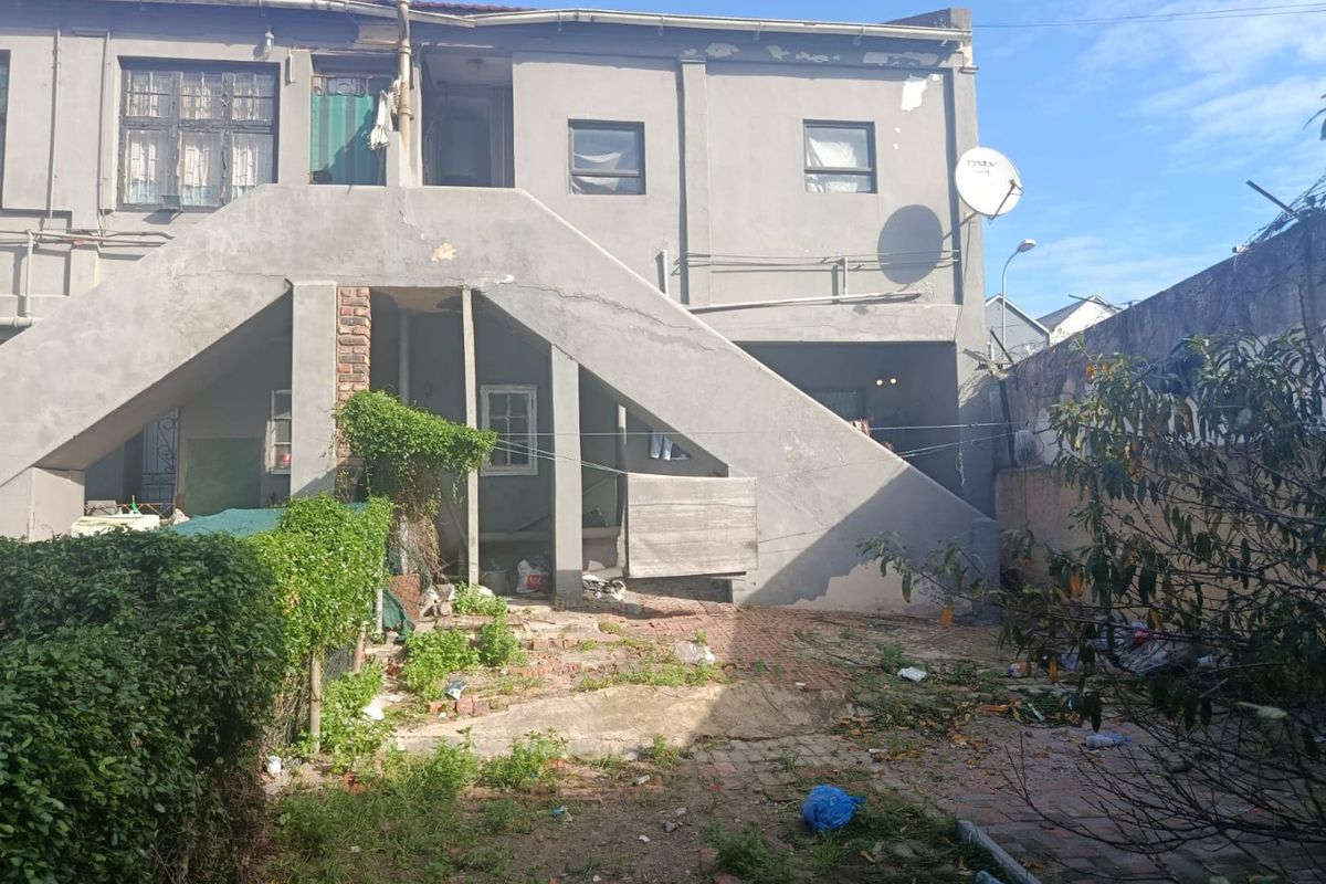 Rear view of a multi-story residential building featuring an external concrete staircase, paved yard area, and boundary wall.