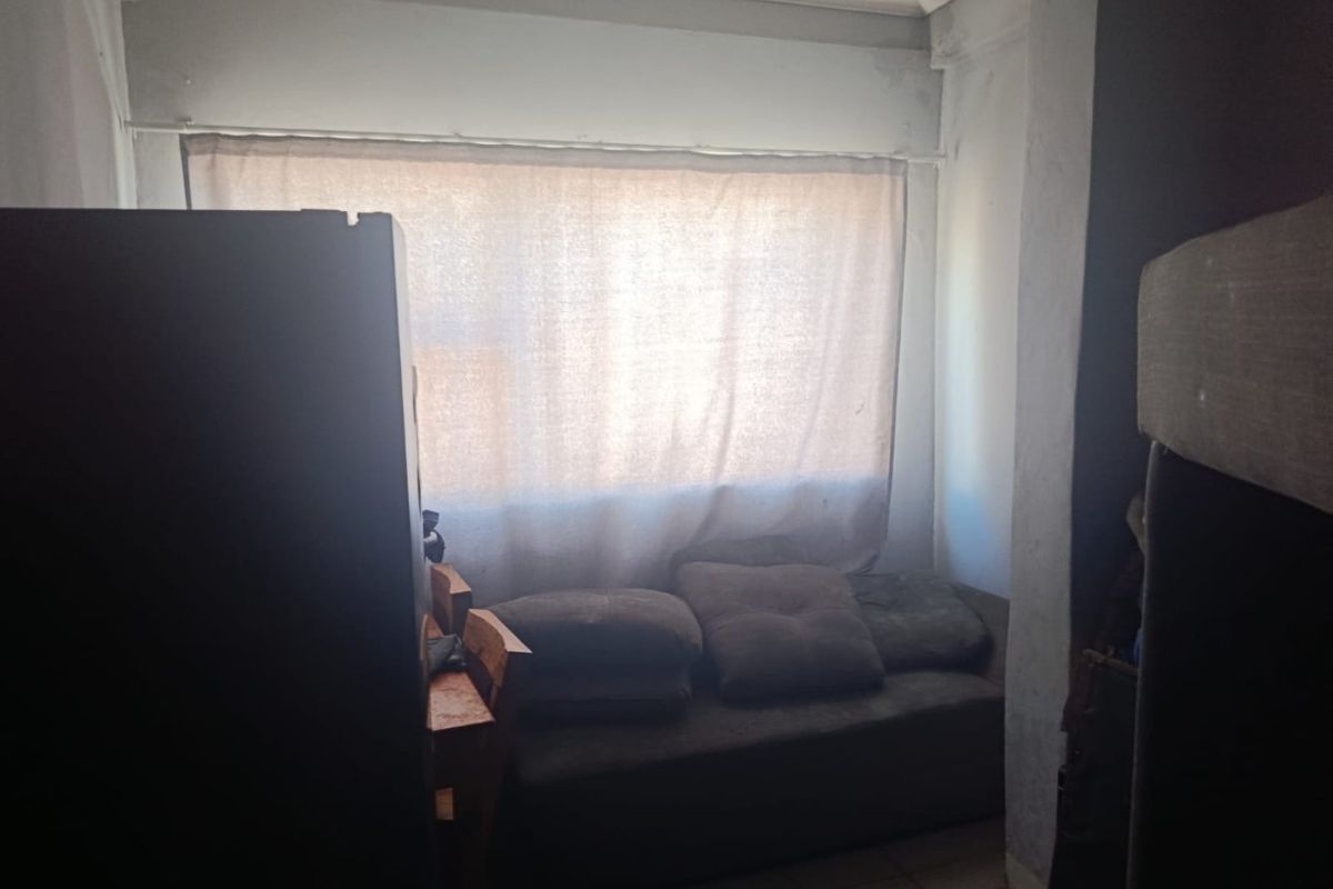 A small bedroom space featuring tiled flooring and a large window, currently requiring cosmetic updates and improved lighting to enhance the room's potential.