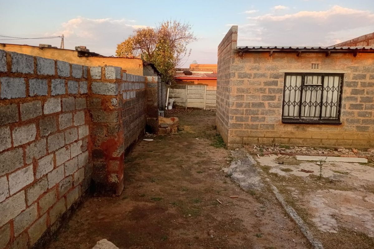 A view of the rear exterior area featuring unfinished brick walls and an unpaved yard space requiring landscaping and maintenance.