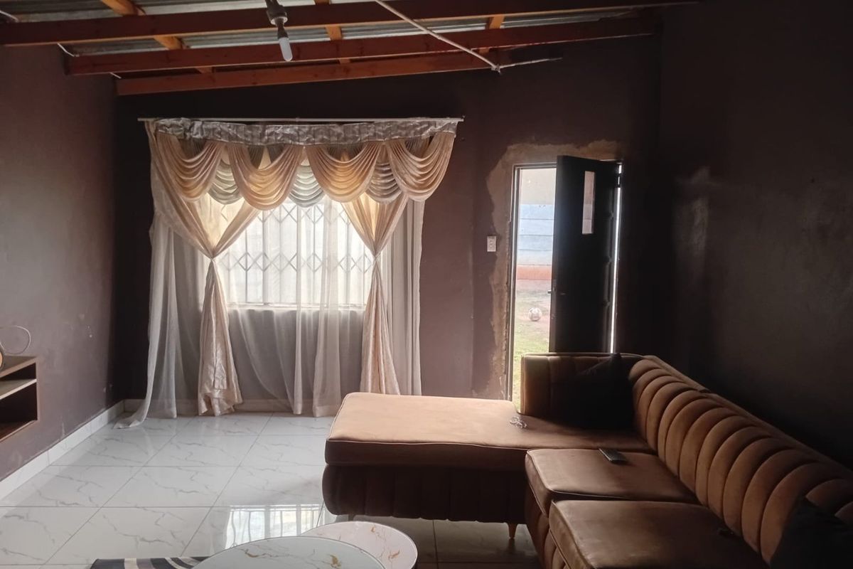 Living room featuring tiled flooring, exposed timber roof rafters, and a doorway leading to the exterior.