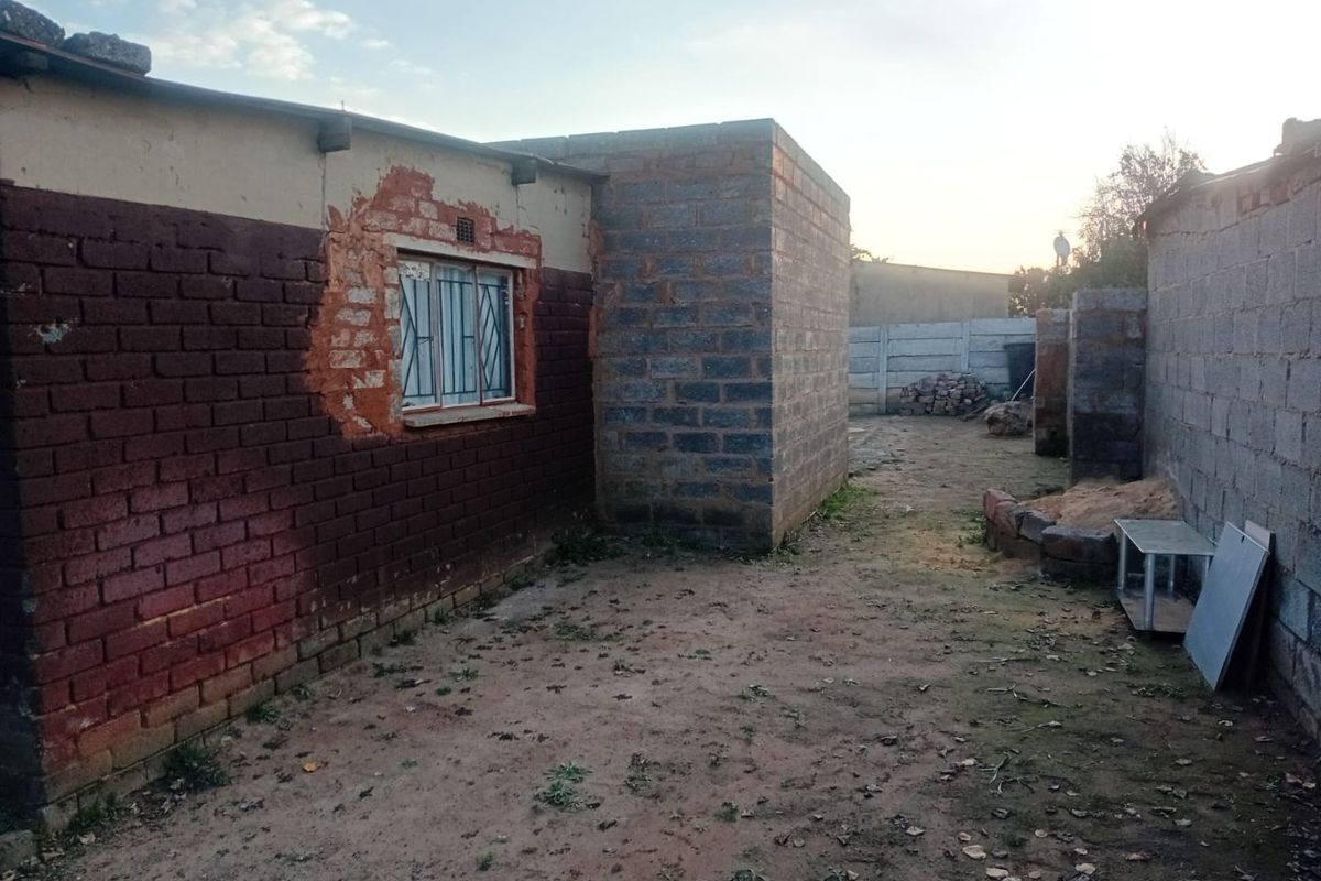 Rear exterior view of the property showing unfinished brick walls, exposed masonry, and a basic yard area requiring landscaping and maintenance.