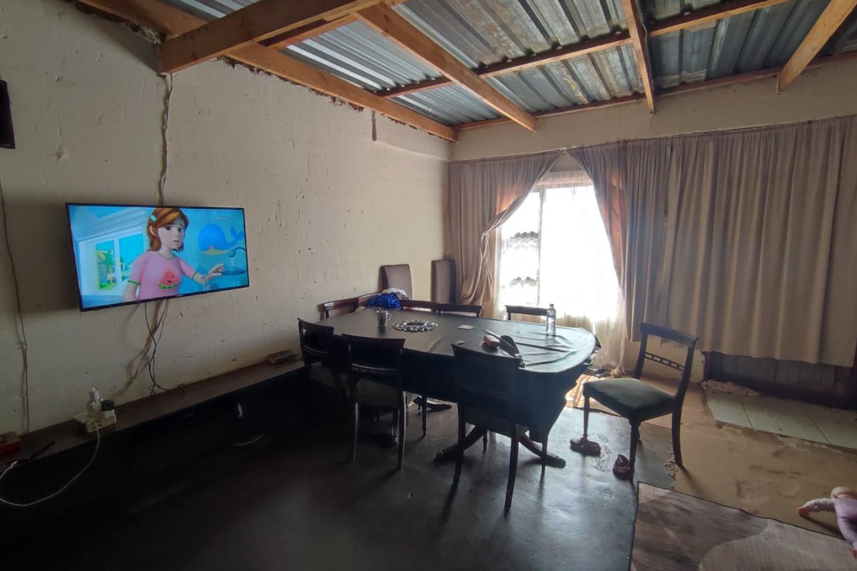 A living and dining area featuring an exposed timber roof structure, unfinished walls, and basic flooring, offering potential for renovation and modernization.
