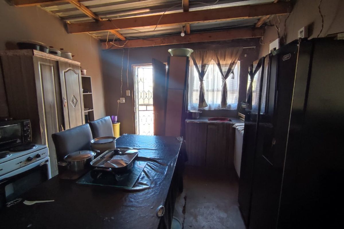 A rustic kitchen area featuring exposed timber ceiling beams, basic cabinetry, and a functional layout with direct access to the exterior.