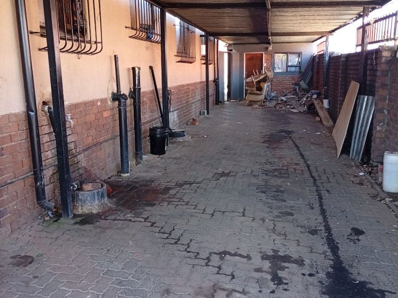 A covered outdoor utility area or side passage featuring paved flooring, brick walls, and metal roofing structure.