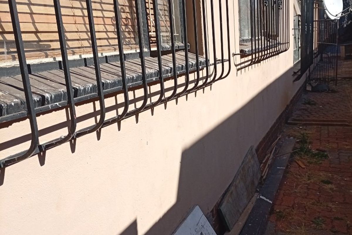 Side exterior view of the house featuring security bars on windows, brick paving, and a satellite dish mounted on the wall.