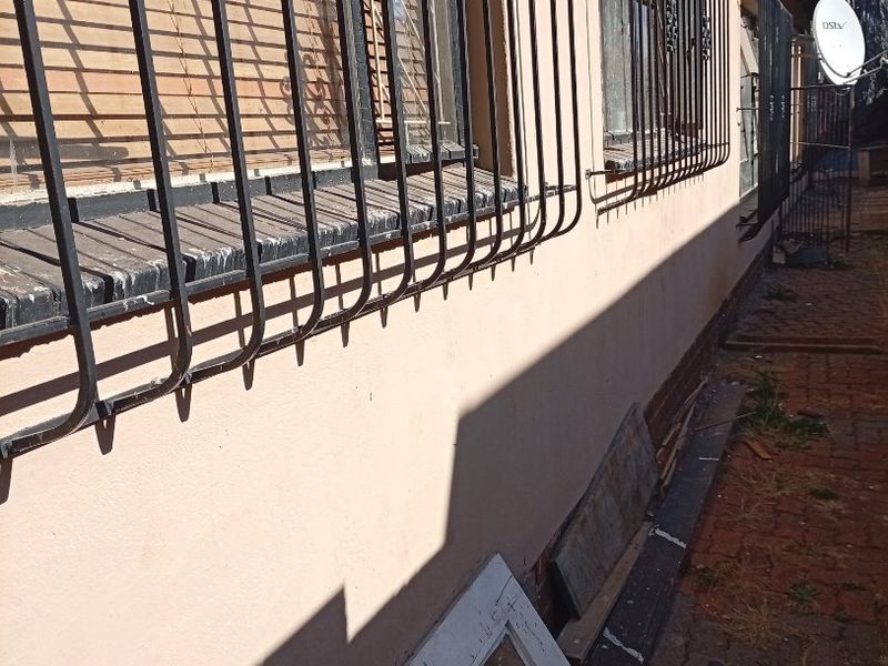 Side exterior view of the house featuring security bars on windows, brick paving, and a satellite dish mounted on the wall.