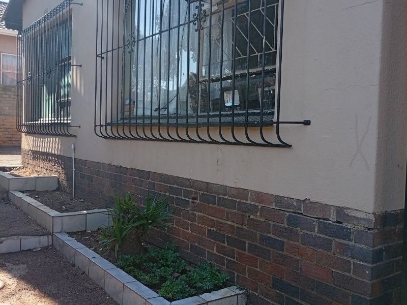 Exterior view of the property facade featuring security bars on windows and a tiered brick garden bed with tiled edging.