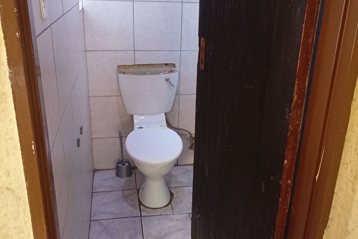 A small, functional guest toilet featuring tiled walls and flooring, currently missing the cistern lid.