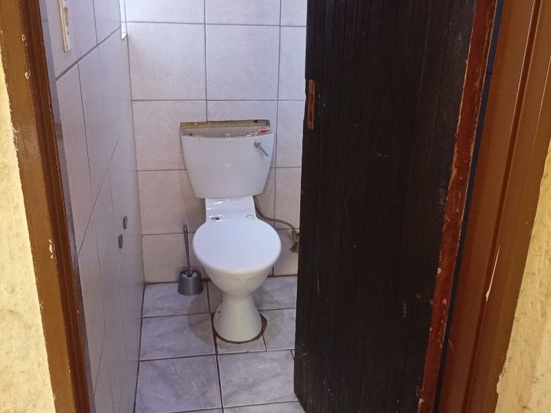 A small, functional guest toilet featuring tiled walls and flooring, currently missing the cistern lid.