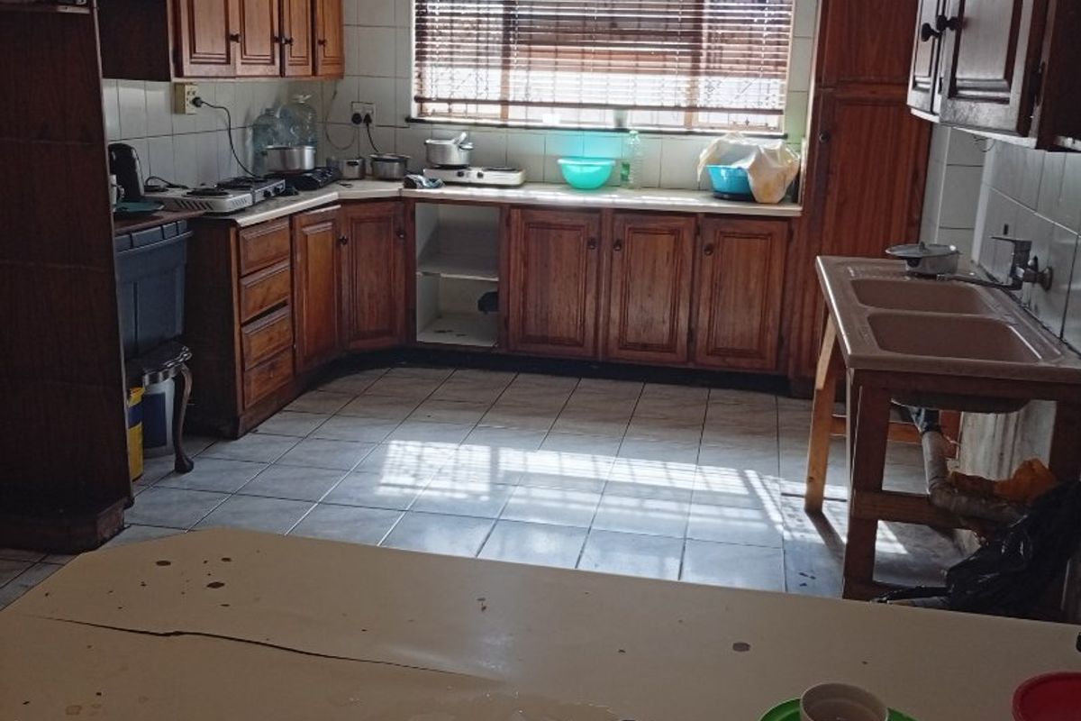 A dated kitchen featuring wooden cabinetry, tiled flooring, and a double basin sink. The space requires modernization to improve functionality and aesthetic appeal.