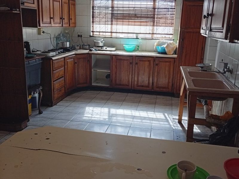 A dated kitchen featuring wooden cabinetry, tiled flooring, and a double basin sink. The space requires modernization to improve functionality and aesthetic appeal.