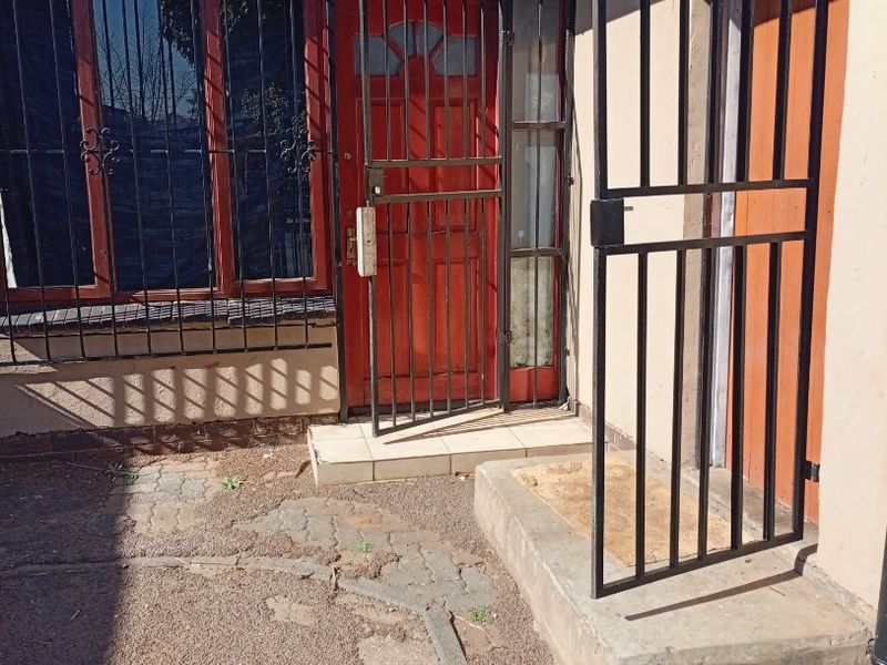 Exterior view of the home entrance featuring security gates, a red front door, and paved walkway area.
