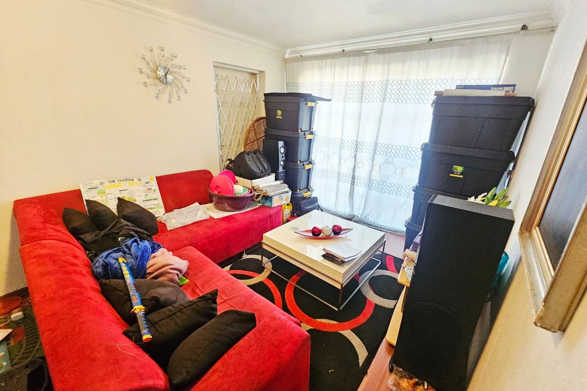 A living room space featuring a large window with sheer curtains and a security gate, providing natural light to the area.