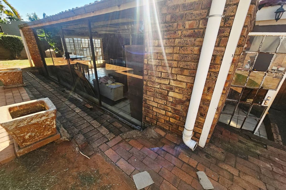Exterior view of the rear brick facade featuring large glass sliding doors, a paved patio area, and exposed downpipe infrastructure.