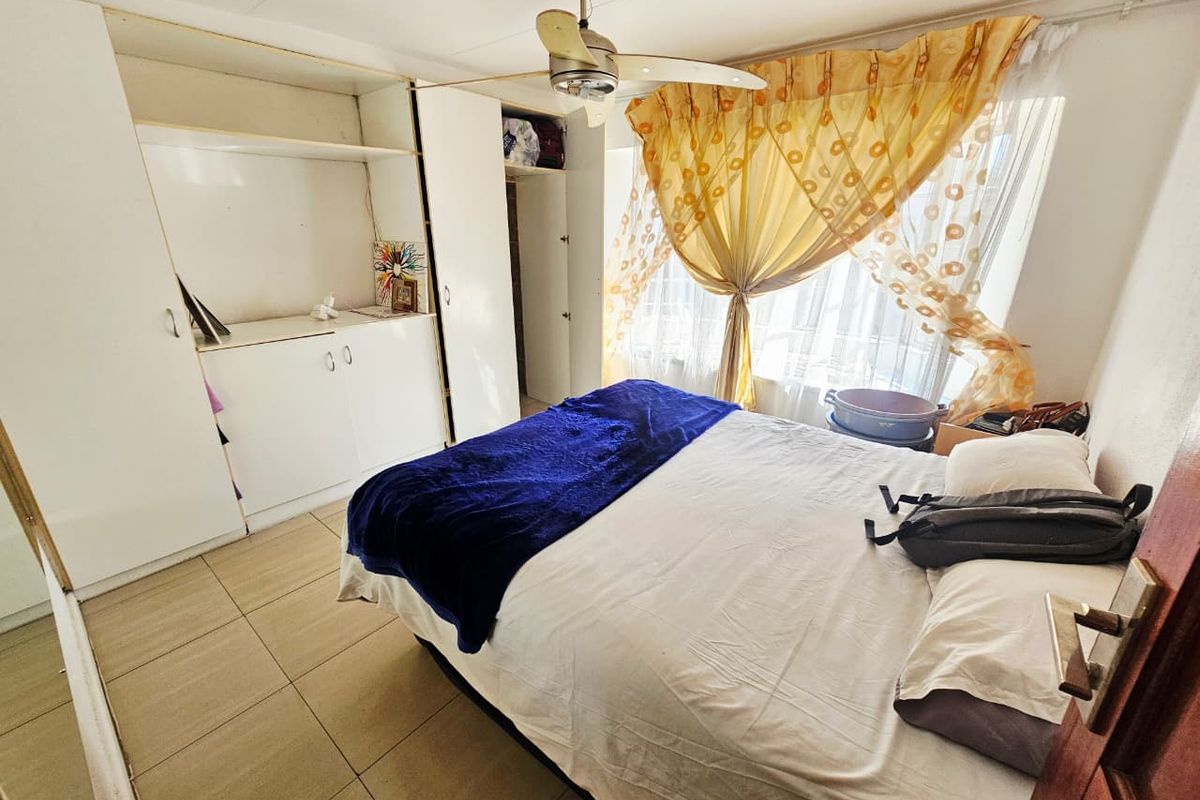 A functional bedroom featuring built-in white cabinetry, tiled flooring, and a ceiling fan, offering a practical layout with natural light.