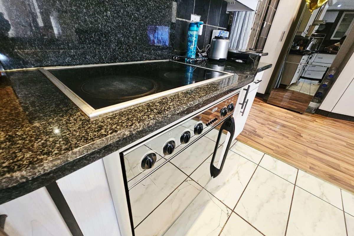 A kitchen area featuring a built-in electric stove and oven with granite countertops and tiled flooring.