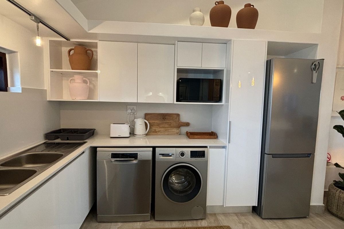 Modern kitchen featuring white high-gloss cabinetry, integrated stainless steel appliances, double sink, and sleek countertops in a clean, functional layout.