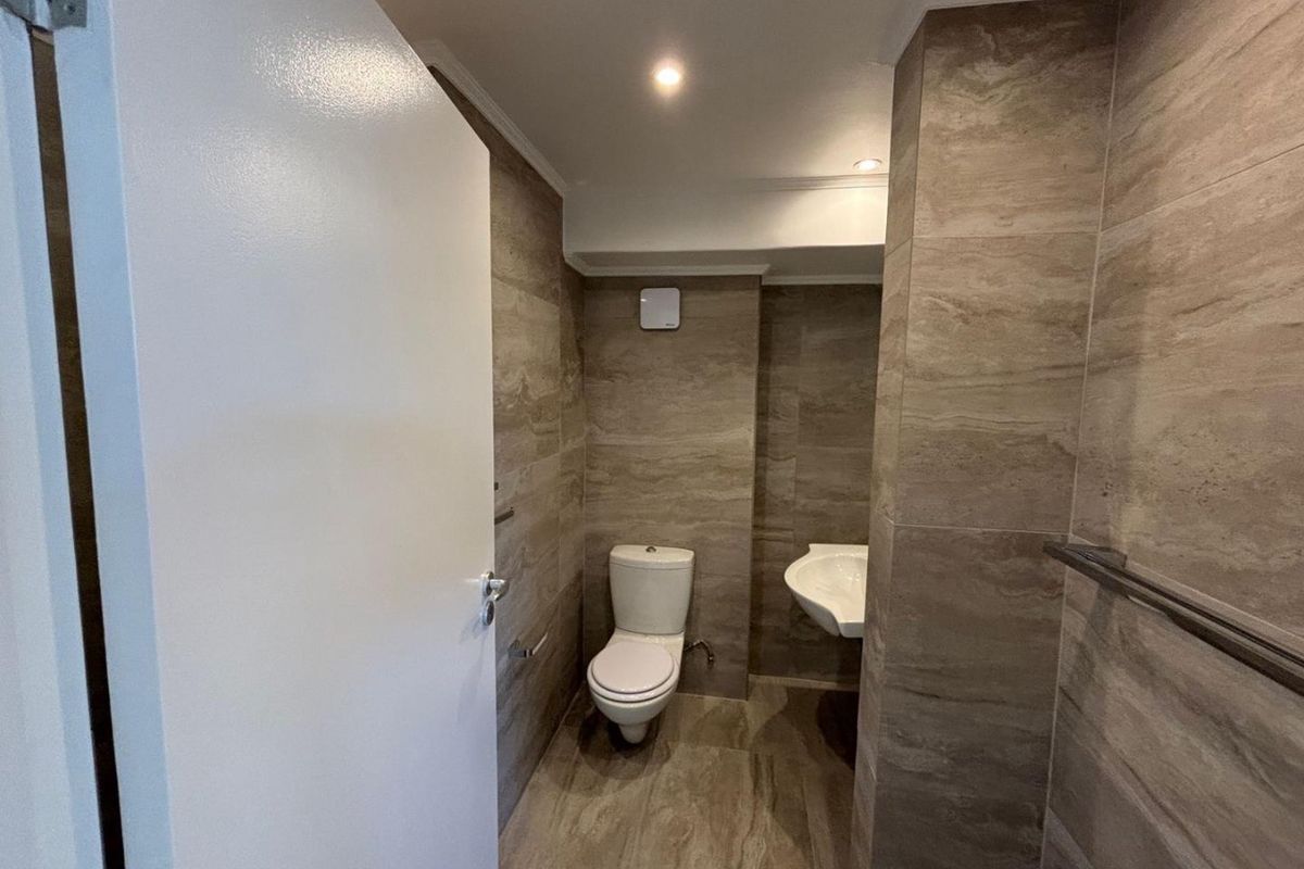 A modern bathroom featuring floor-to-ceiling stone-look tiling, a wall-mounted basin, and a standard toilet suite.