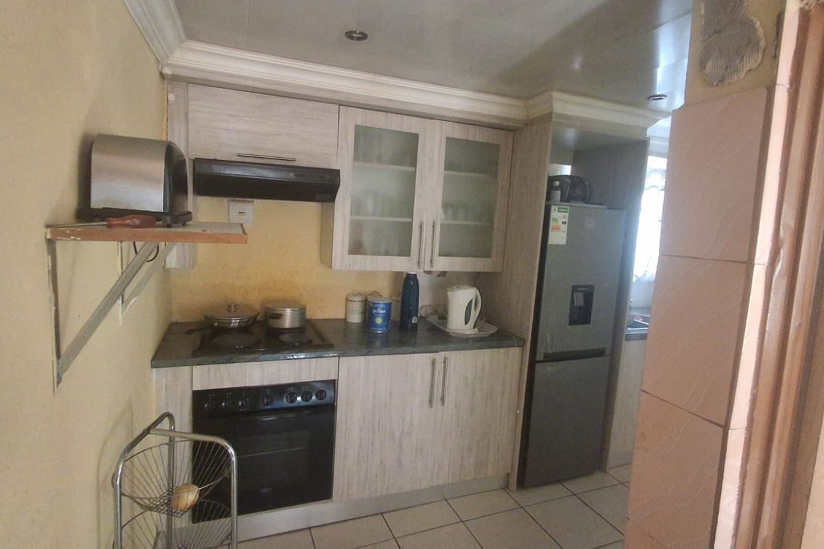 A compact kitchen featuring built-in cabinetry, a fitted oven and hob, extractor fan, and tiled flooring.