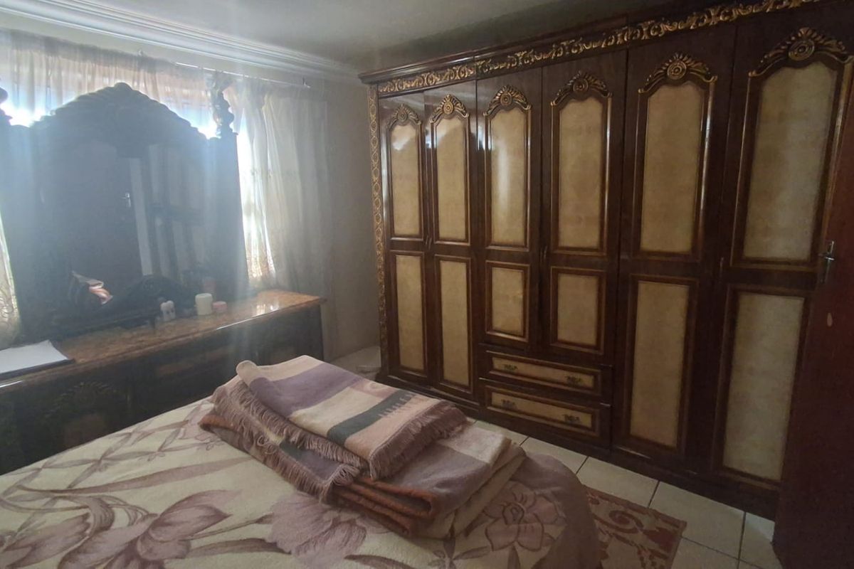 A bedroom featuring tiled flooring and a large built-in wooden wardrobe with decorative detailing.