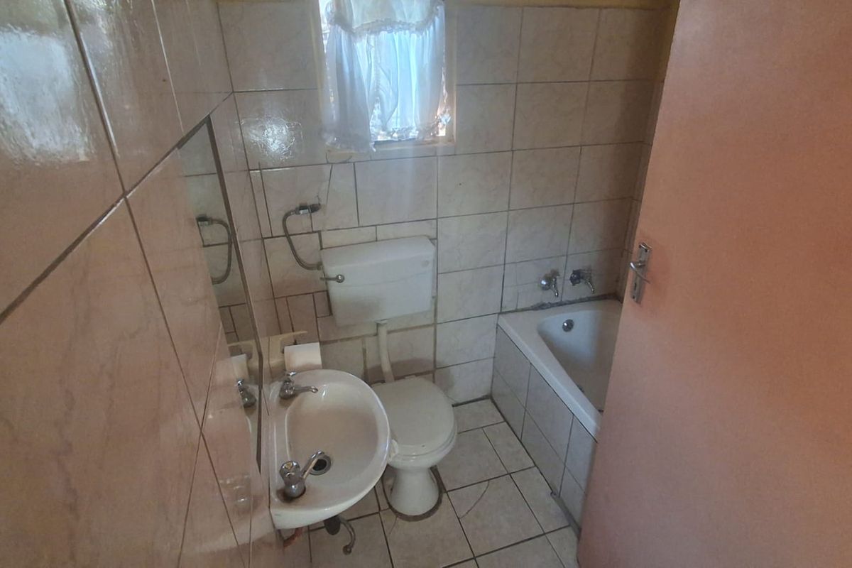 A compact bathroom featuring a built-in bathtub, pedestal basin, and toilet with full-height wall tiling.