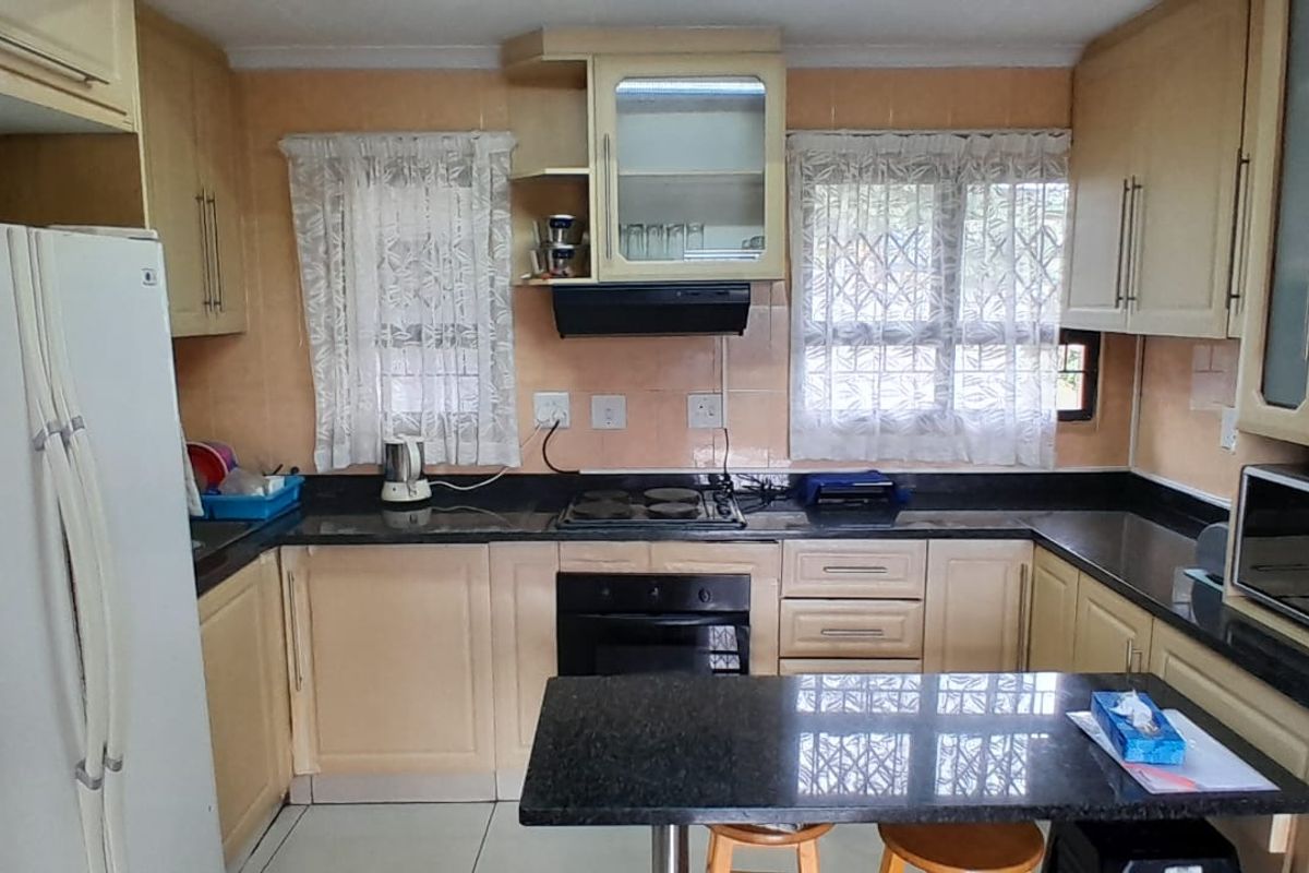 A functional kitchen featuring U-shaped cabinetry, dark granite countertops, a built-in oven, and a hob with an extractor fan.