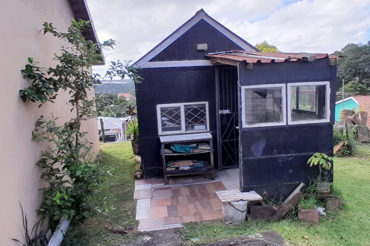 A detached outbuilding or utility structure featuring dark exterior cladding, a small covered entrance area, and a garden setting.
