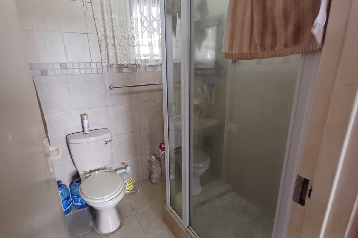A compact bathroom featuring a shower enclosure, toilet, and tiled walls. The space is functional but dated, offering potential for modernization.