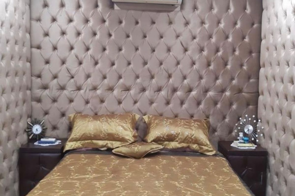 A well-appointed bedroom featuring extensive tufted velvet wall paneling and a wall-mounted split-system air conditioning unit.