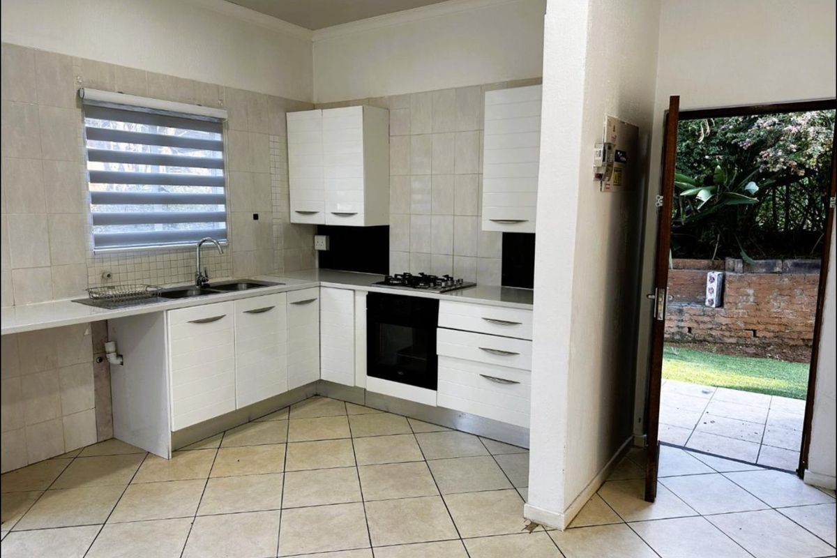 A functional kitchen featuring white cabinetry, a built-in oven and hob, tiled splashbacks, and direct access to an outdoor patio area.